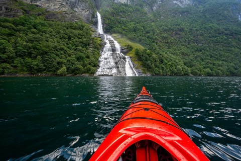 Kayak trip on the Geirangerfjord at the Freier waterfall, tip of a red kayak in the fjord,