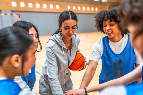 Female basketball coach motivating and inspiring her team during a time out, holding the ball and