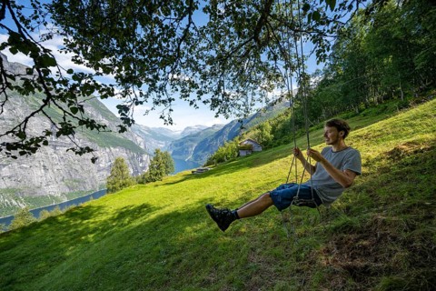 Young man swinging, Blomberg Gård, historic mountain farm with grass roof on a steep mountainside