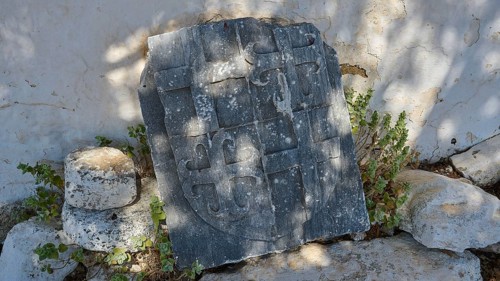 Ancient tombstone with inscriptions, surrounded by vegetation and shade, Church of Agia Paraskevi,