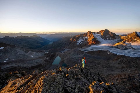 Mountaineer in front of picturesque high mountain landscape at sunrise with alpenglow, blue glacial