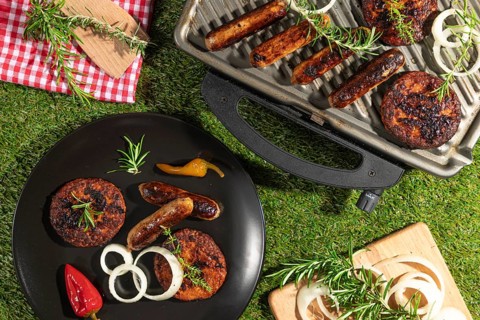 Grilled sausages and burgers on a barbecue and plates with rosemary on a green lawn