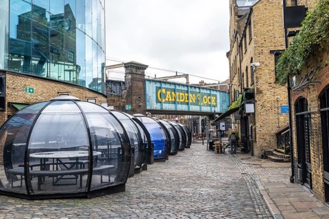 Transparent dining pods line a cobblestone street beneath the camden lock bridge in london,
