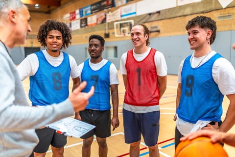 Coach holding clipboard explaining game strategy to his basketball team players wearing training