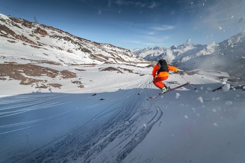 An athlete male skier jumps from a snow-covered slope against the backdrop of a mountain landscape