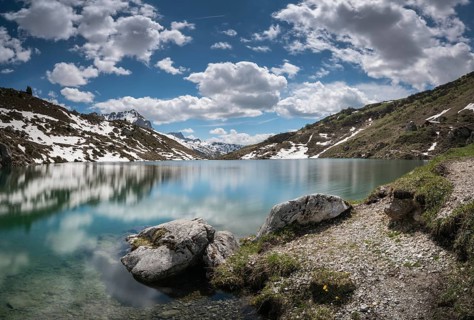 gorgeous mountain lake in the Alps with reflections and snow remnants under a blue sky with white