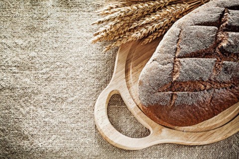 Carving board bread rye ears on burlap background