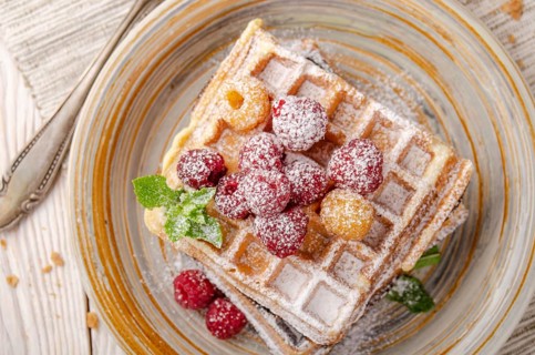 Flat lay view at Belgian waffles served with raspberries and mint leaf dusted with powdered sugar