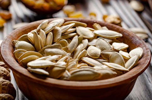 Pumpkin seeds in wooden bowl on kitchen table food background