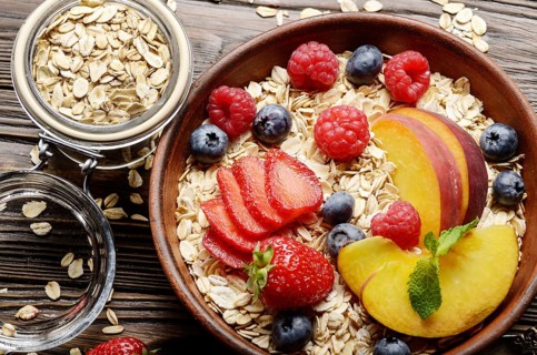Flat lay of fruit healthy muesli with peaches strawberry almonds and blackberry in clay dish on