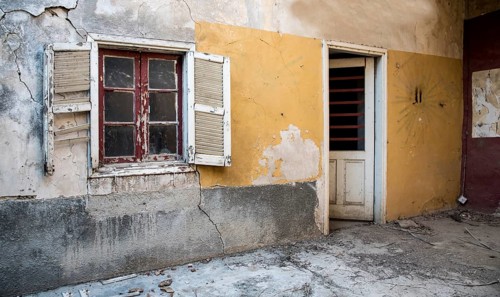 Backyard of a deserted abandoned house with a broken closed window and door and with yellow cracked