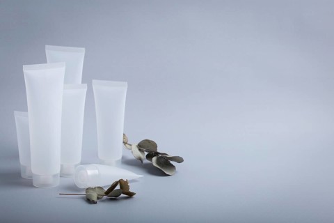 White empty plastic cosmetic tubes staying at gray background with eucalyptus branches, concept of