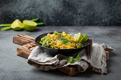 Asian vegetarian noodles with vegetables and lime in black rustic ceramic bowl, wooden chopsticks