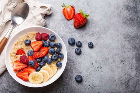 Oatmeal porridge with fruit and berries in bowl with spoon on gray stone background table top view,