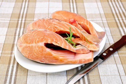 Three pieces of trout in white plate with rosemary on a checkered cloth background