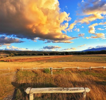 The huge cloud lit yellow-orange rays of sunset. Cozy wooden bench by the side of the road in
