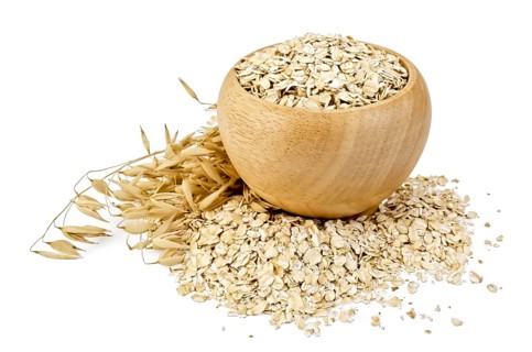 Oat flakes in a wooden bowl, oat stalks, oat flakes scattered on the table, against a white