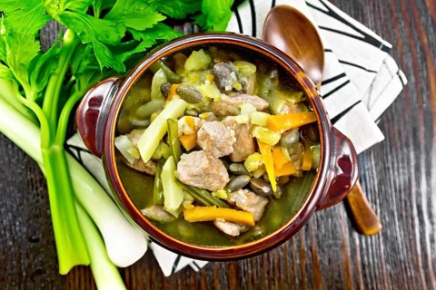 Eintopf soup of pork, celery, beans, carrots and potatoes with leek in a clay bowl on a towel on