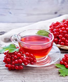 Tea with viburnum in a glass cup, wicker plate with berries, green leaves and burlap on wooden