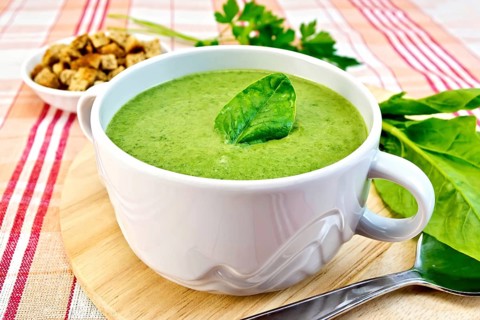 Green soup puree in a bowl with green leaf spinach, spoon on the board, croutons, parsley on a
