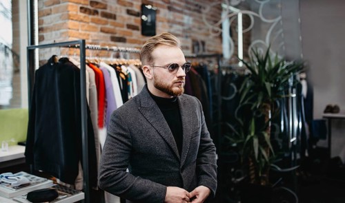 Man wearing sunglasses and a coat stands inside a chic clothing store with trendy decor