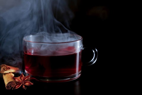 Steaming cup of hot tea with star anise and cinnamon stick isolated on black background and copy