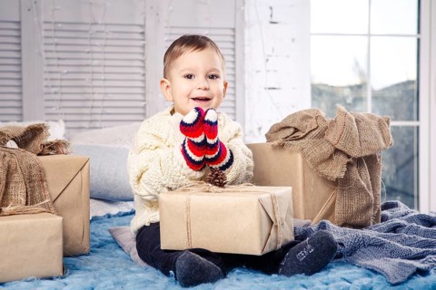 Little funny playful boy a child sits on a bed on Christmas day with gift boxes in white wool
