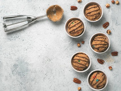 Safe-to-eat raw monster cookie dough in small portion bowl, ice cream scoop and nuts on gray cement