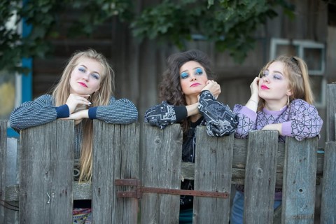 Three funny village girls are standing near the old village fence. Bored country girls