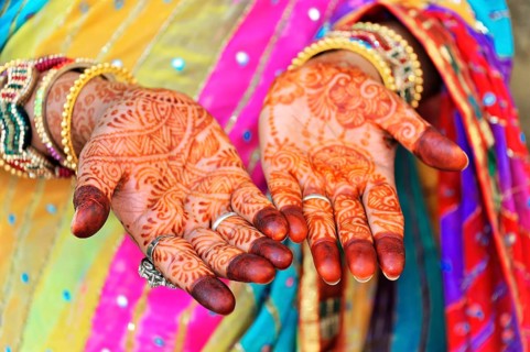 Close-up of painted hands with elaborate mehndi designs, accompanied by colourful robes, Rajasthan,