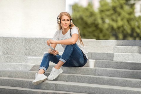 Happy young woman with vintage headphones and a cup of coffee to go, surfing the internet on a