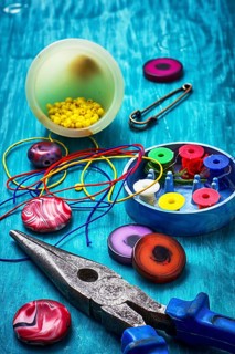 Beads, pliers and other needlework accessories on outdated turquoise wooden background