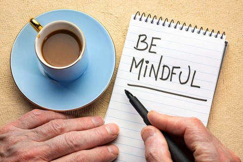 Be mindful - man hand writing a note with a black marker in a spiral notebook