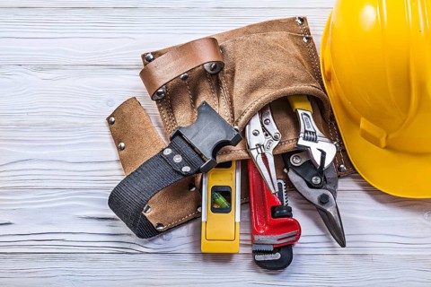 Collection of construction tooling in leather tool belt safety building helmet on wooden board