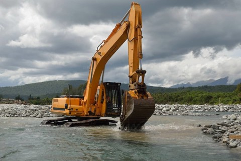 10 ton digger shifting shingle to deepen the channel in a flowing river, Westland, New Zealand,