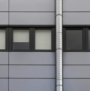 Grey cladding panels on an industrial building with a row of back window frames and a silver pipe