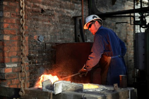 A foundryman clears slag from the molten iron in the furnace