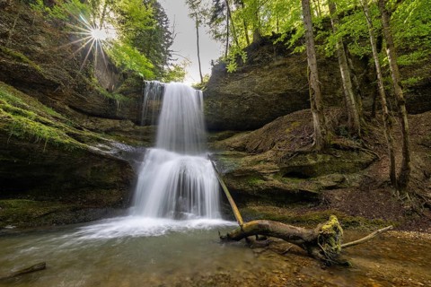 Waterfall with in the forest, where the sun rays penetrate through the trees, forming a peaceful