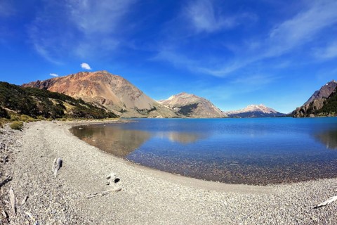 Oval blue lake surrounded by mountains. Mountains reflected in the mirrored water. Picture taken
