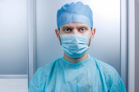 Doctor facing the camera, dressed in mask and scrubs in a clinical setting