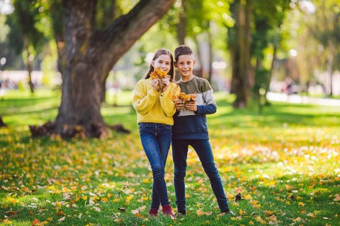 Happy Caucasian siblings enjoying in autumn day in park, sunny weather. Kids having fun holding