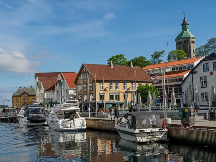 A harbour with several boats in front of colourful buildings under a blue sky with few clouds,