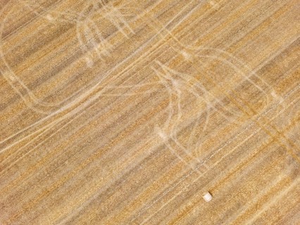 Striking tracks and patterns from a tractor on a dry agricultural field with straw bales, aerial