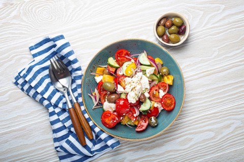 Greek fresh healthy colorful salad with feta cheese, vegetables, olives in blue ceramic bowl on