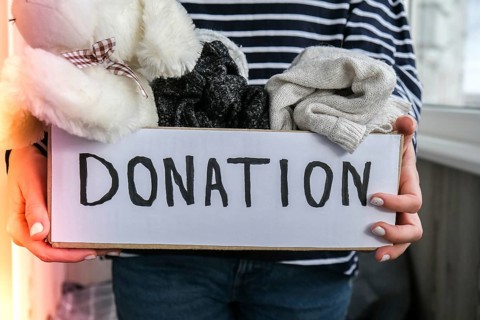Female volunteer holding donation box with old used toys and clothes indoors. Happy Charity.