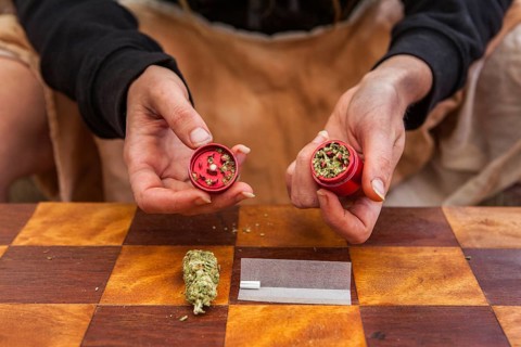Selective focus closeup of person's hands holding a red weed filled grinder shot from above.