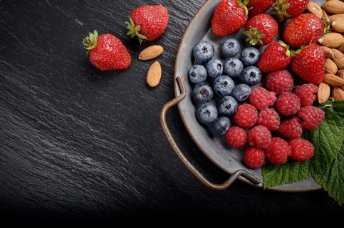 Tray with ripe organic bilberry raspberry strawberry and almonds set on slate closeup