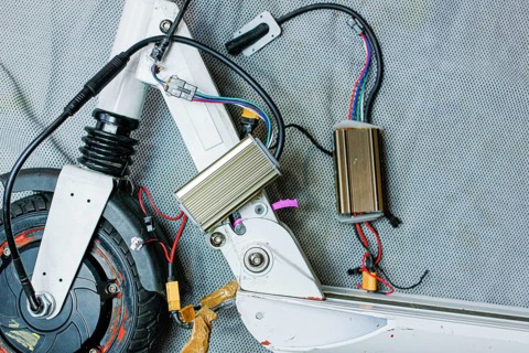 Electric scooter with exposed components and wiring, showcasing mechanical details on a grey