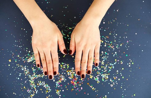 Top view of crop anonymous female with bright manicure over dark blurred background with colorful