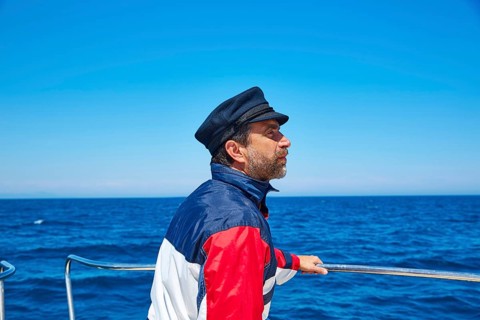 Beard sailor man sailing sea ocean in a boat with captain cap looking horizon